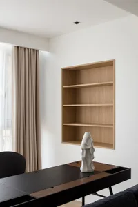 A minimalist living room featuring a wooden shelving unit with a white ceramic sculpture on a black and brown wooden table.