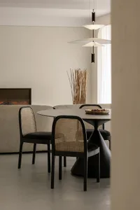 A modern minimalist dining area with a round table, wicker chairs, and a fireplace.