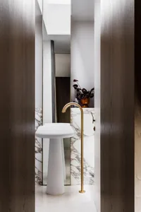 Modern bathroom with a white pedestal sink, gold faucet, and marble wall.