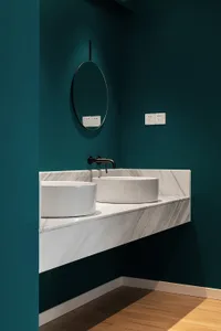 Modern bathroom featuring a marble countertop with two sinks, white walls, and wooden flooring.