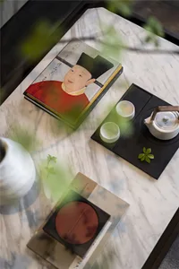 A modern coffee table setting with marble top, featuring a teapot, cups, books, and decorative greenery.