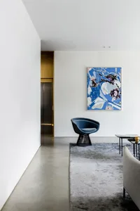 A modern living room with a blue armchair, a colorful abstract painting, and a concrete floor.