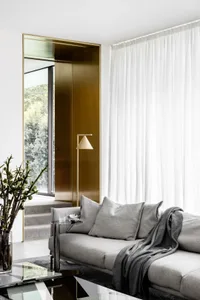 Modern living room with a gray sofa, white curtains, and a brass floor lamp.