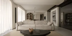 Modern, minimalist living room featuring neutral-toned furniture and decor, large windows with white curtains, and a simple c