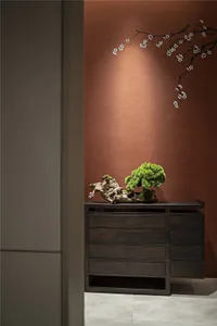 A wooden console table with a bonsai tree and a decorative branch on a textured brown wall.