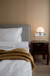 Bedroom featuring minimalist design with a grey headboard, white linens, and a mustard yellow throw blanket.