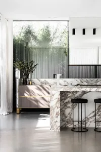 A modern minimalist kitchen with a marble countertop and black stools.