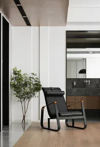 Minimalist design living room featuring a black leather chair, wooden flooring, and a potted plant.