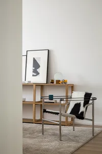 A minimalist living room with a wooden armchair and a shelf with framed artwork.