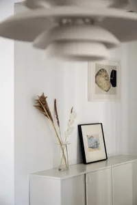 White minimalist wall decor with a vase of dried plants and a framed black and white abstract piece.
