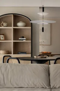 Modern minimalist dining room featuring a round table with wicker chairs, a wooden shelving unit, and a pendant light fixture