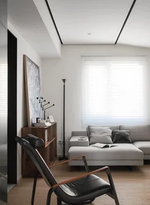 Minimalist living room with a gray sectional sofa, black leather chair, and wood floor.