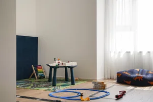 A modern playroom featuring a wooden table surrounded by toys and a large floor pillow with animal prints.