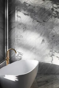 Modern bathroom with marble walls and floor, featuring a freestanding bathtub with a gold faucet.