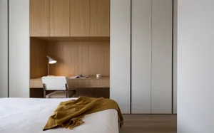 Modern minimalist bedroom featuring a wooden desk and chair, minimalist light fixtures, and a bed with a yellow blanket.