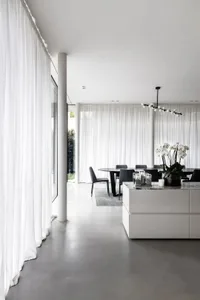 A modern minimalist dining room with white curtains, black furniture, concrete floors, a glass chandelier, and a marble dinin