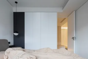 Modern minimalist bedroom with white cabinets and a bed with a neutral-colored blanket.