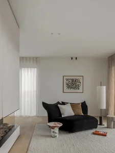 A minimalist living room featuring a black sofa, marble side table, and textured cotton curtains with concrete flooring and a