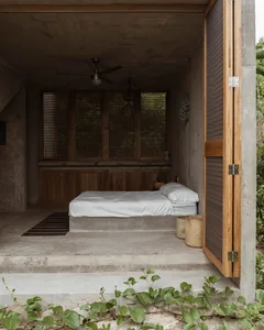 A minimalist bedroom with a concrete platform bed, white bedding, and wooden window shutters.