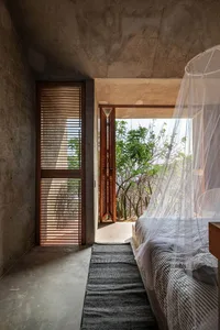 A minimalist bedroom with concrete flooring, wooden shutters, and a large bed covered in a white curtain.