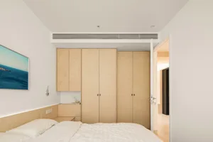 A minimalist bedroom featuring wood cabinets and a bed with white sheets and pillows.