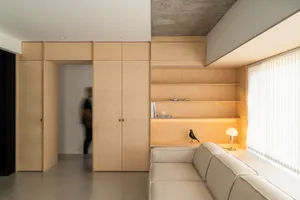 A minimalist living room featuring wood storage units and a beige sofa.