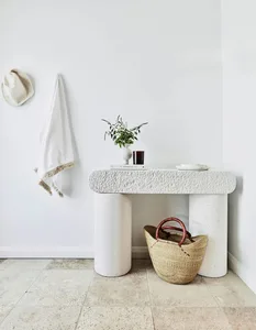 A modern console table made of concrete with a white vase containing flowers and a woven basket underneath it.