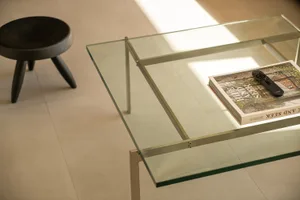 Modern glass coffee table with minimalist design, featuring clear glass top and metal legs, styled with a book and remote con