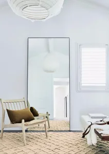 A minimalist living room with white walls, wooden furniture, and a large mirror.