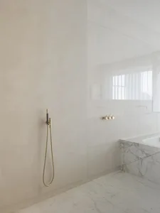 Modern minimalist bathroom design with marble floor and walls, featuring a sleek walk-in shower with brass fixtures.