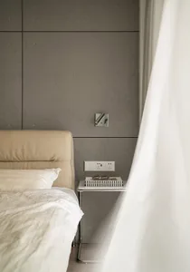 A minimalist bedroom featuring a bed with a beige leather headboard and a nightstand with a book, glasses, and power outlets 