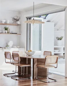 A modern minimalist kitchen featuring a wooden table and chairs, a glass pendant light, and decorative shelving.