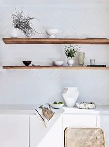 A modern minimalist kitchen with wooden shelves, white marble countertops, and ceramic vases and bowls.