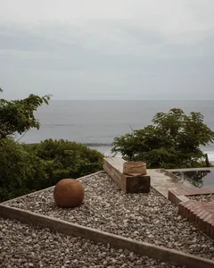 A granite patio with a view of the ocean, featuring a wooden bench, a spherical object, and a woven basket.