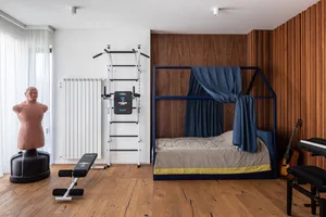 A minimalist bedroom with a blue canopy bed, wooden walls, and exercise equipment.