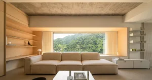 Modern minimalist living room featuring a beige sectional sofa, wooden shelves, concrete ceiling, and a large window overlook