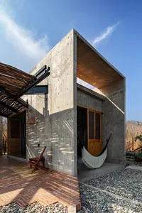 A modern house with concrete exterior featuring a hammock and a wooden door.