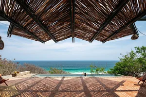 A person relaxing in a pool overlooking the ocean with a wooden and concrete structure.