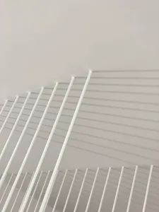 A close-up view of a metallic grid air vent on a white wall.
