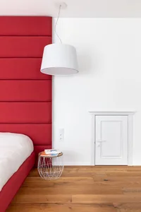 Minimalist bedroom with red upholstered headboard on a wooden floor.