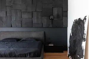 A minimalist bedroom featuring dark wooden panels on the wall, a gray bed, and a black and white abstract painting.