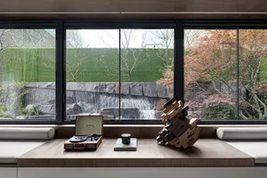 A minimalist living room with wooden furnishings and stone accents, featuring a small table with a record player, books, and 