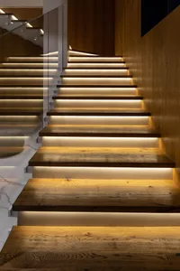 A modern staircase featuring wooden steps with recessed lighting on the underside of each tread for illumination.