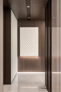 A modern corridor featuring a paneled wall with diagonal lines, illuminated by concealed lighting.