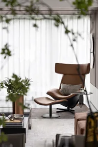 A modern living room with a cozy brown leather armchair and ottoman, featuring minimalistic decor and plush cushions.
