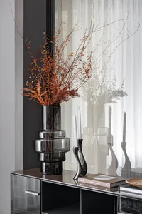 A modern shelf decorated with a tall black vase containing dried flowers, a black bottle, and books.