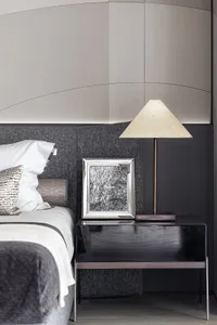 A modern bedroom featuring a black side table with a white lamp, a white bed with a black headboard, and a black and white pi
