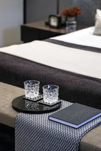 A detailed view of a modern bedroom featuring a neatly made bed with a black and white patterned textile, two crystal glasses