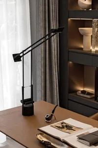 A modern minimalist office setup with sleek black desk lamp, wooden pipe, leather-bound book, and open notebook.