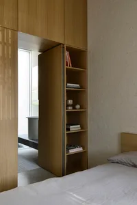 A minimalist bedroom with a wooden bed and built-in shelves against a white brick wall.